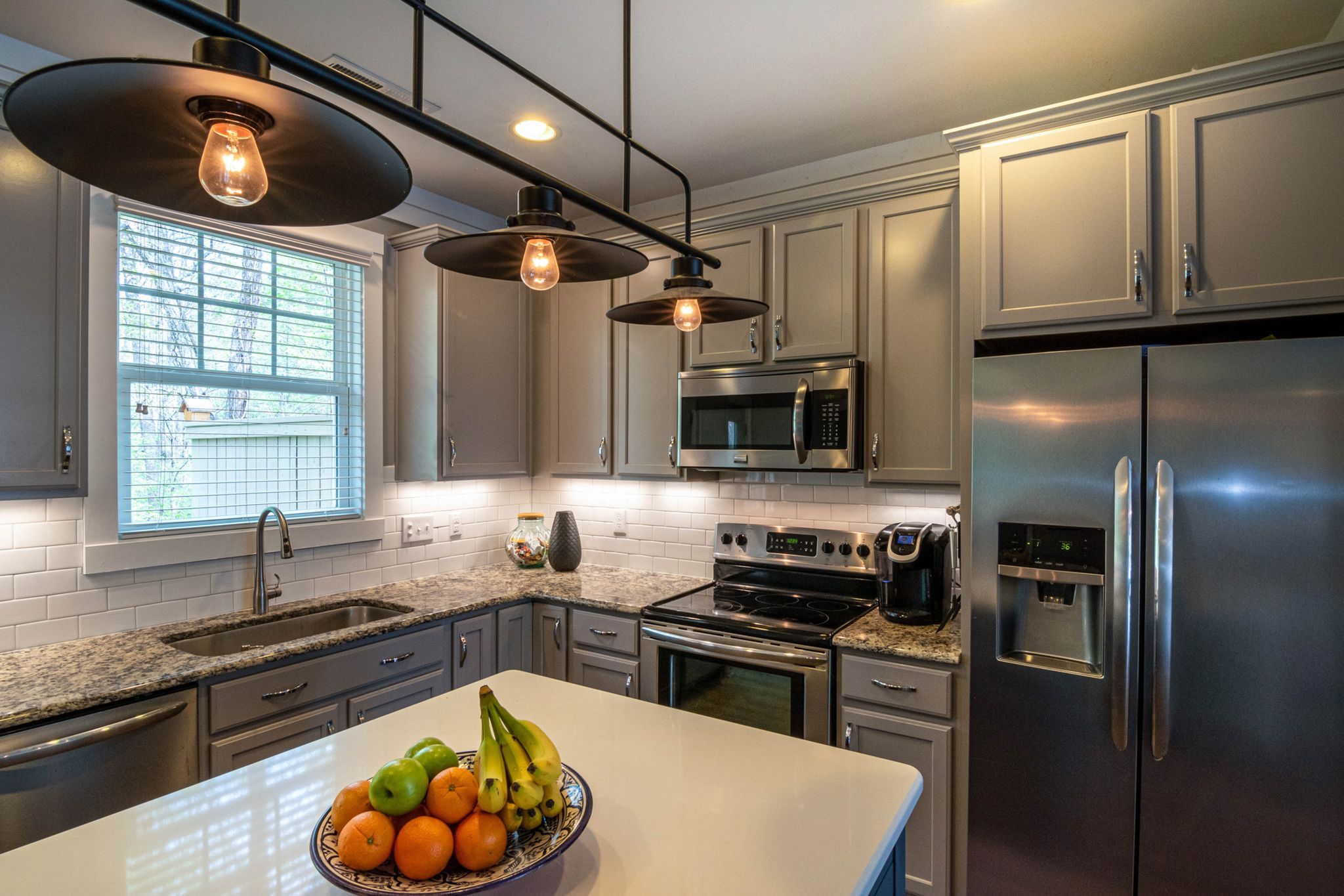 Contemporary kitchen featuring a bowl of fruits, stainless appliances, and elegant lighting.